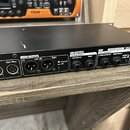 Záběr na zadní panel černého elektronického zařízení v rackovém provedení. Panel obsahuje MIDI konektory In a Out / Thru, dva MIXER OUTPUTS (Left, Ri…