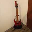 Elektrická kytara s červeně-černým přechodovým lakem a hnedým hnedobéžovým hmatníkem. Kytara má dva humbuckery a je umístěna na černém stojanu u bílé…