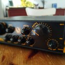 Detailní pohled na přední panel černého elektronického zařízení s oranžovými popisky. Jsou vidět ovládací knoflíky a nápisy LIMITER, MASTER, MAX, MUT…