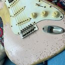 Detail elektrické kytary s růžovým lakem a bílým pickguardem. Na ovládacích knoflících jsou nápisy VOLUME a TONE. Lak je výrazně opotřebovaný, s četn…