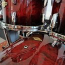 Detailní pohled na červené bubny s tmavě rudým mramorovaným povrchem a chromovaným kováním. Na korpusu je vidět oválný zlatý štítek s nápisem Masters…