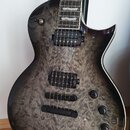Elektrická kytara s tmavě šedým průhledným lakem a výraznou strukturou dřeva na topu. Nástroj má dva humbuckery, jeden tónový potenciometr a přepínač…