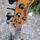 Záběr na hlavu pětistrunné basové kytary z přírodního dřeva s černými ladicími kolíky. Na zadní straně hlavy je černý nápis ERNIE BALL MUSICMAN Sting…