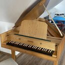 Dřevěné piano s otevřeným víkem a hudebním pultem v přirozené barvě dřeva. Nad klávesnicí je vyryt nápis AMMER. Nástroj vykazuje známky používání a o…