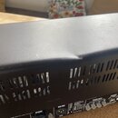 Detailní pohled na horní hranu a zadní panel černého kytarového komba. Na horní části je viditelný výrazný promáčknutýv hnutý povrch. Na zadním panel…