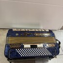 Modrá harmonika s texturovaným povrchem a žlutými měchovými lištami. Na horní části je nápis DELICIA a ve spodní části štitek s textem MELODIA VII. N…