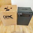 Černý basový kombozesilovač s rukojetí na horní straně a ovládacím panelem v zadní části. Vedle něj stojí hnědý kartonový obal s velkým logem GK a ná…
