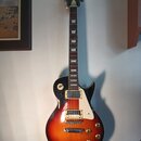 Elektrická kytara s tvarem Les Paul v barevné variantě sunburst (černá, červená a žlutá). Na hlavě je vidět nápis Epiphone. Nástroj má dva humbuckery…