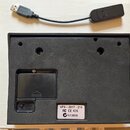 Fotografie zachycuje spodní stranu černého elektronického zařízení a USB kabel s ovladačem. Na spodní straně přístroje je bílá nálepka s nápisy VP4 -…