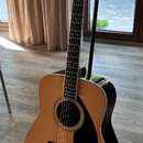 Akustická kytara v přirozené dřevěné barvě s černým plechtrem a černým kobylníkem. Na hlavě hmatníku je bílý nápis YAMAHA a dekorativní ornament. Nás…