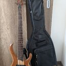 Elektrická basová kytara s přírodním dřevěným povrchem a hnědým hmatníkem. Na hlavě nástroje je viditelné logo Ibanez. Součástí je černý polotvrdý po…
