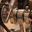 Detailní záběr na kovový mechanismus s řetězem a ozubeným kolem v chromovaném povrchu. Na okraji ozubeného kola je vyražen nápis "MADE IN TAIWAN". Po…