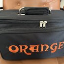 Černý textilní přepravní kufr s rukojetí a zipy. Na přední straně je oranžový vyšívaný nápis ORANGE. Povrch textilie vykazuje mírné znečištění a opot…