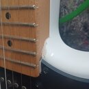 Detailní záběr na spoj hmatníku a těla bílé elektrické kytary. Na hraně bílého laku v místě styku s hmatníkem je viditelný odlak a trhlina v materiál…