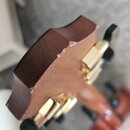 Detailní pohled na hřbet hlavy kytary z hnědého dřeva se zlatými ladičkami a černými knoflíky. Na horní hraně hlavy je viditelné odloupení laku a poš…