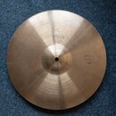 Kruhový mosazný činel s viditelným broušením povrchu. Na povrchu jsou vyraženy nápisy „PAISTE 505“ a „MEDIUM HI-HAT TOP“. Povrch vykazuje drobné škrá…