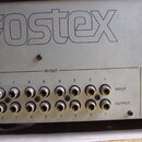 Detail zadní strany stříbrného elektronického zařízení s velkým nápisem Fostex. V sekci IN/OUT se nachází 16 konektorů typu jack, rozdělených do dvou…