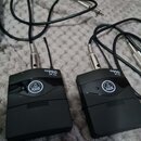 Dvě černé bezdrátové vysílače s připojenými kabely a jack konektory. Na obou zařízeních je bílý nápis MINI PRO PT 40 a logo AKG v kroužku. Povrch pla…