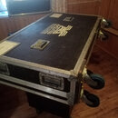 Černý transportní flightcase s hliníkovými hranami a kovovým kováním, osazený čtyřmi modrými kolečky. Na horní části je bílý nápis „ACULTES“ a logo v…