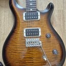 Elektrická kytara s dvojcutem, s hnědým plamenovitým topem a tmavými okraji. Je vybavena dvěma humbuckery, chromovaným mostem a dvěma oválnými potenc…