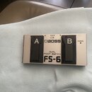 Stříbrný dvoupedálový spínač s černými plasty. Na horní straně je logo BOSS a nápisy DUAL FOOT SWITCH oraz FS-6. Pedály jsou označeny písmeny A a B,…