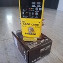 Žlutý loop pedal NUX LOOP CORE umístěný na své originální krabici. Zařízení má černý ovládací panel s nápisy USB, DC 9V, SAVE DELETE, STOP MODES a RH…