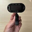 Černý klipový ladič s oválným tvarem, který drží ruka. Na přístroji jsou nápisy FLAT, PITCH, ITEM/U, CLIP a MIC, v dolní části je model AT-370B TUNER…
