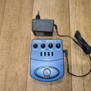 Modrý kytarový procesor s nápisem V-TONE GUITAR GDI 21 GUITAR AMP MODELER - DRIVER - DI. Zařízení má čtyři ovládací knoflíky s popisky DRIVE, TREBLE,…