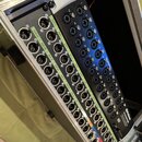 Audio rozhraní v hliníkovém transportním kufru. Zařízení obsahuje řadu vstupů XLR a jack, s nápisy AUX 1 až AUX 24. V pravém dolním rohu je vidět log…