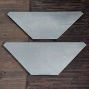 Dvě stříbrné kovové desky trapezoidního tvaru položené na dřevěné podlaze. Povrch desek vykazuje drobné škrábance a známky opotřebení. Na deskách nej…
