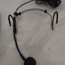 Černý headset s mikrofonem a čepicí v podobě pěnové clony. Zařízení má tenký kovový rám s ohýbatelným ramenem mikrofonu a připojovací kabelem. Na pře…