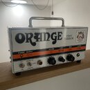 Kytarový zesilovač značky Orange, model Tiny Terror, v bílém provedení s kovovou rukojetí. Na předním panelu je velký černý nápis ORANGE a menší text…