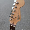 Hlava elektrické kytary z přírodního světlého dřeva s hnedým hmatníkem. Na hlavě je černý nápis Fender® STRATOCASTER MADE IN U.S.A. a sériové číslo S…