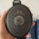 Černá sluchátka s kulatými mušlemi a kovovou mřížkou přes reproduktory. Na horním plastovém prvku je bílý štítek s nápisy HG SAX a Jubilee. Povrch pl…