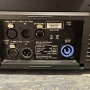 Fotografie zachycuje zadní panel černého elektronického zařízení s různými konektory a popisky. Jsou zde vidět porty označené jako OUT, IN, ETHERNET…