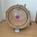 Fotografie zobrazuje basový buben s béžovou koženou membránou a chromovaným obručováním. Na membráně je nahoře logo REMO s nápisem FIBERTONE a uprost…