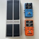 Na fotografii jsou tři efektové pedály. Vlevo je stříbrný kovový pedalboard s nápisem BOSS a čtyřmi velkými černými spínači. Vpravo nahoře je modrý p…