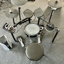 Elektronická bicí souprava s černým rámem a padami. Na snare drumu je vidět nápis Roland a V-Drums, na činele vlevo je nápis Roland. Součástí je ovlá…