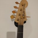 Fotografie zachycuje hlavu basové kytary z přírodního světlého dřeva s pěti zlatými ladicími mechanismy. Na dřevě je černý nápis Fender PRECISION a d…