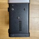 Záběr na zadní stranu černého elektronického zařízení s horní částí v stříbrné barvě. Na černém povrchu jsou vidět čtyři křížové šrouby a řada vertik…