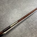 Detailní záběr na část hrdla nebo tětivy hudebního nástroje. Je vidět kombinace tmavého dřeva a stříbřitých kovových prstenců. Povrch vykazuje mírné…