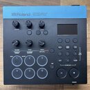 Černý trigger modul s modrým horním panelem. Na modré části je bílý nápis Roland TRIGGER MODULE TM-6 PRO. Zařízení obsahuje displej, několik otočných…
