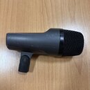 Černý dynamický mikrofon s mřížkou v horní části. Tělo je vyrobeno z matního tmavého materiálu a obsahuje integrovaný držák. Povrch vykazuje drobné š…