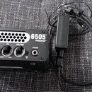 Černý kytarový zesilovač s nápisy Peavey, 6505 PIRANHA. Na předním panelu jsou tři ovládací knoflíky s popisky GAIN, EQ (pod nimi NOTCH a FULL) a VOL…