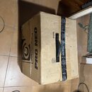 Kartonový přepravní box hnědé barvy s černou plastovou rukojetí. Na boku je velký černý nápis PRO NEO a logo Thomann, na čelní straně je svisle napsá…