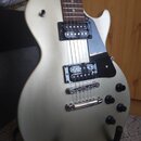 Elektrická kytara s bílým matným povrchem korpusu a černým hmatníkem. Nástroj má dva humbuckery s černými rámečky, černý plechtr ochránič a čtyři ovl…