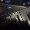 Detailní záběr na ovládací panel černého elektronického nástroje. Jsou vidět tlačítka s modrými nápisy TEMPO, F1, F2 a ENTER, tlačítko ON/OFF, modrá…