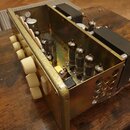 Fotografie zachycuje vnitřek elektronického zařízení, pravděpodobně lampového zesilovače, v kovovém šasi. Uvnitř jsou vidět čtyři elektronky, transfo…