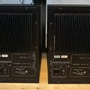 Zadní strana dvou černých studiových monitorů. Na spodním panelu obou zařízení je bílý štítek s nápisy P11, R-7982, HIGH GAIN, ROOM EQ > 6 kHz, ROOM…