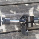 Černý kovový stojan nebo držák s teleskopickým vysuvným mechanismem. Na konci se nachází plastový utahovací knoflík a pěnová krytka. Povrch je v dobr…